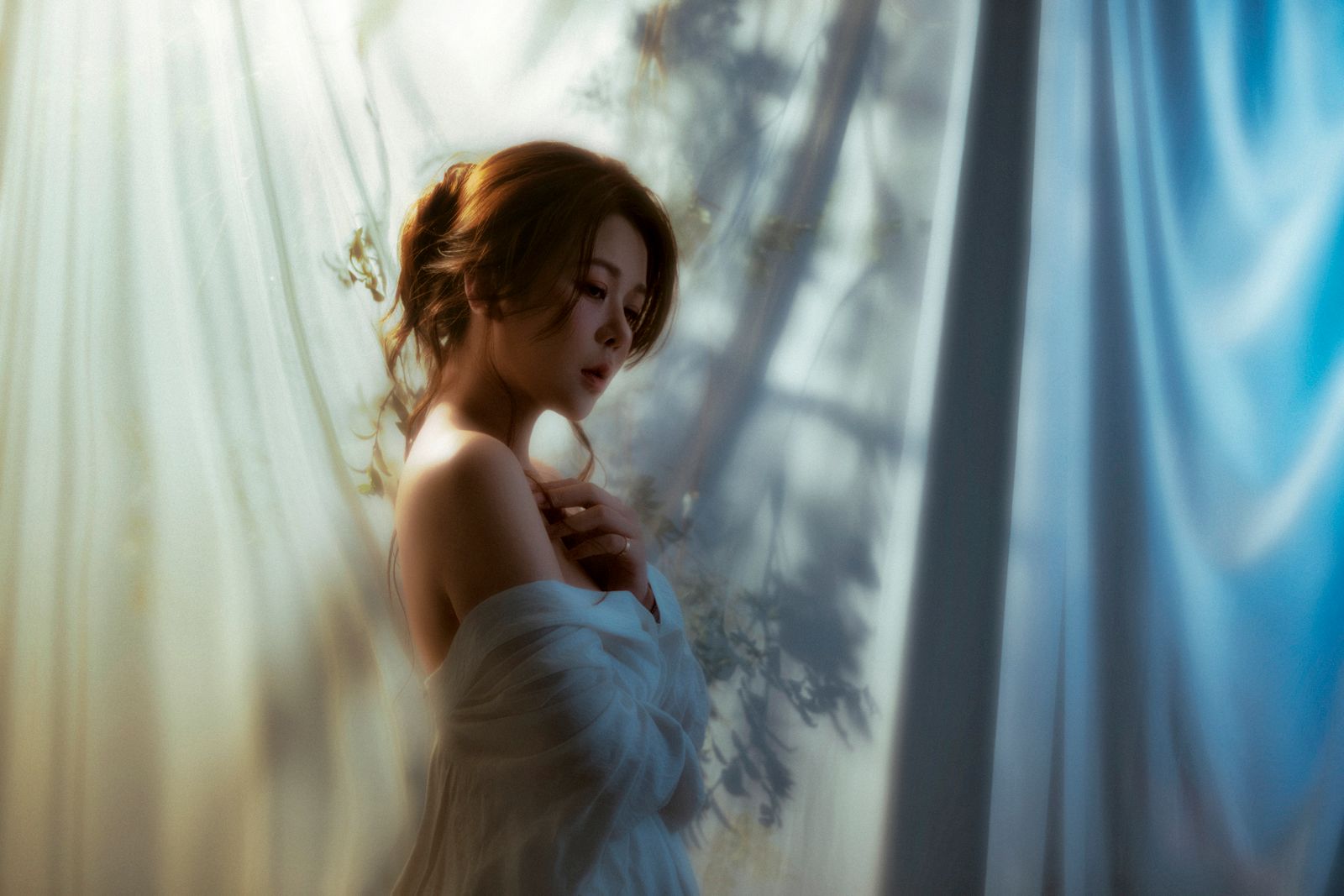 Portret artistic al unei femei în lumină visătoare, cu umbre pe un fundal drapat